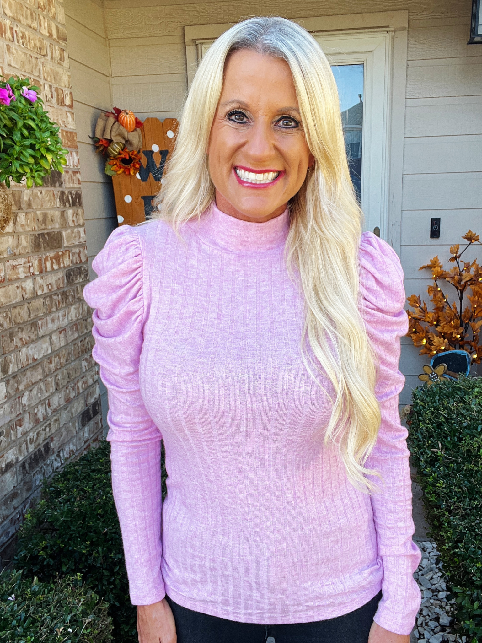 Woman wearing a light purple turtleneck sweater standing outside a house.