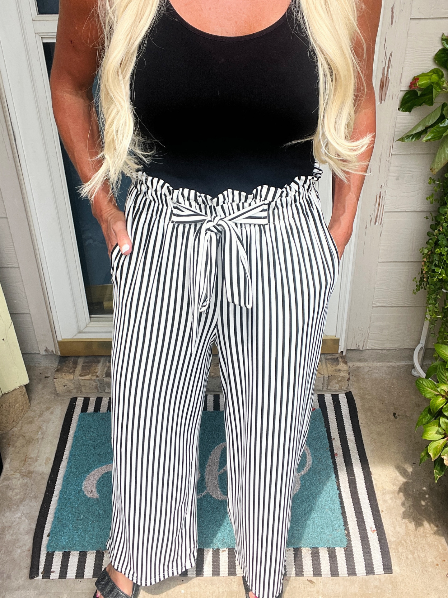 Person wearing a black top and black and white striped pants on a porch.
