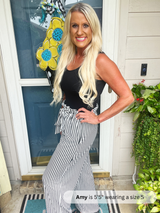 Woman standing in front of a door with a decorative flower, wearing a black top and striped pants.