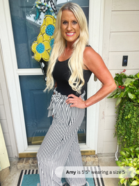Woman standing in front of a door with a decorative flower, wearing a black top and striped pants.