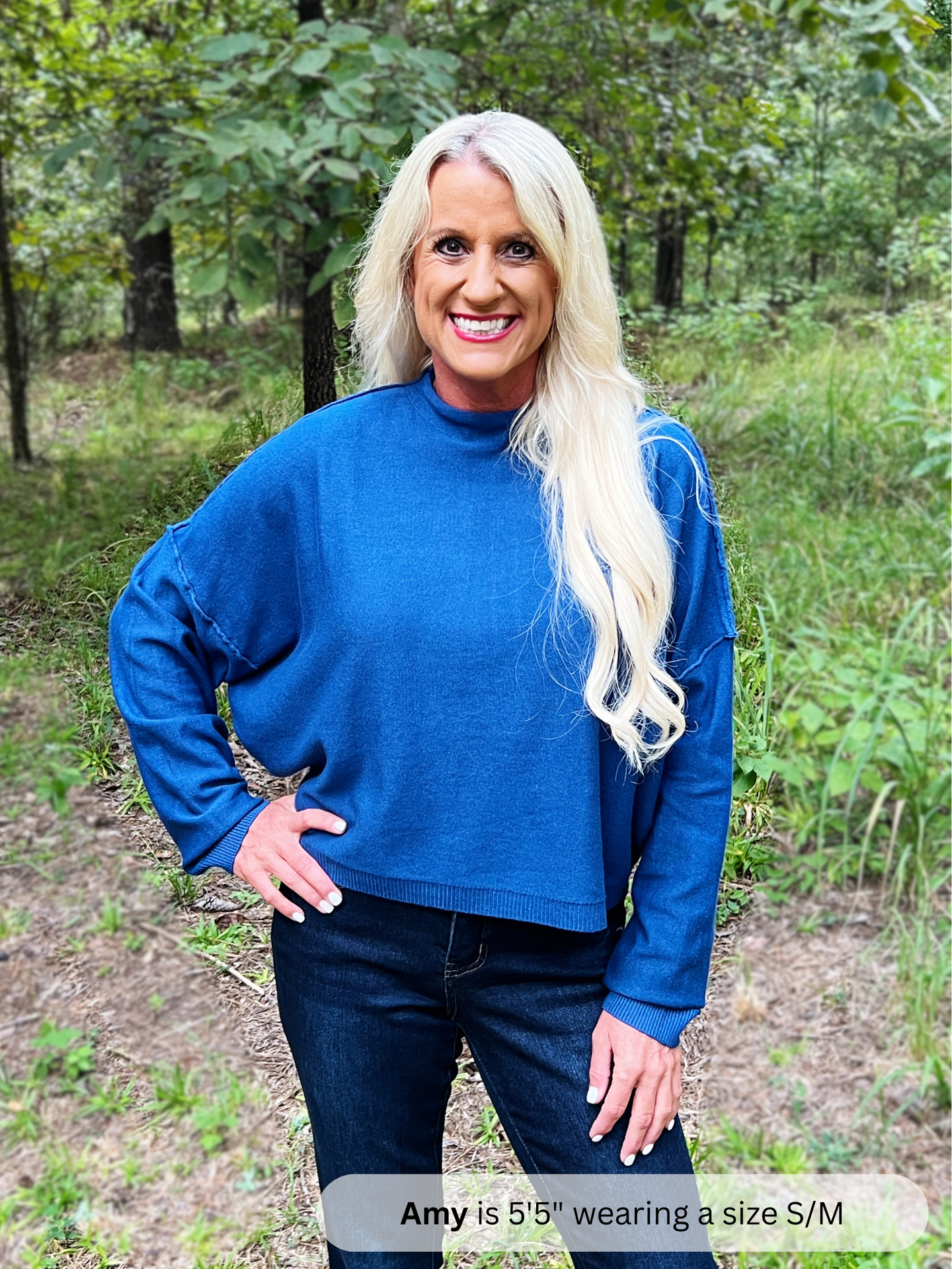 Woman wearing a blue sweater and jeans standing in a forest