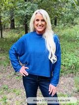Woman wearing a blue sweater and jeans standing in a forest