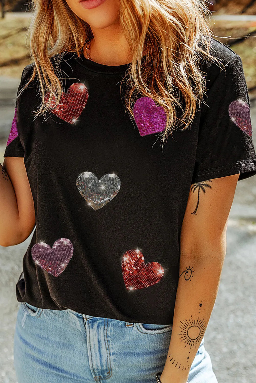 Person wearing a black t-shirt with colorful heart patterns outdoors