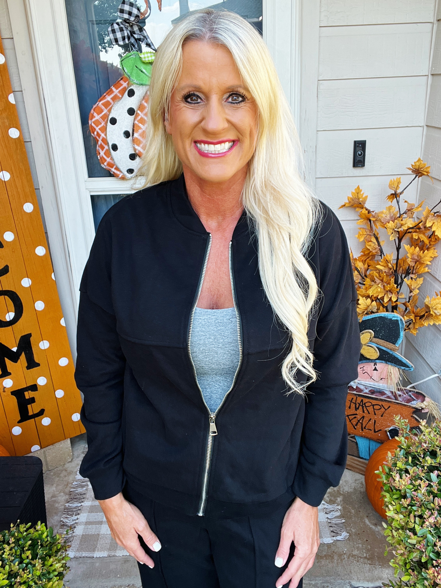Woman in black jacket standing in front of a decorated door with 'Home' and 'Happy Fall' signs.