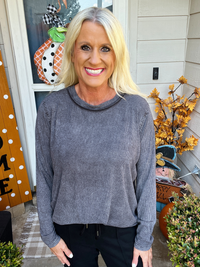 Woman wearing a gray sweater standing in front of a decorated door with pumpkins and autumn decorations.