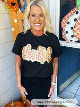 Woman wearing a black t-shirt with 'thankful' printed on it, standing in front of a door with Halloween decorations.