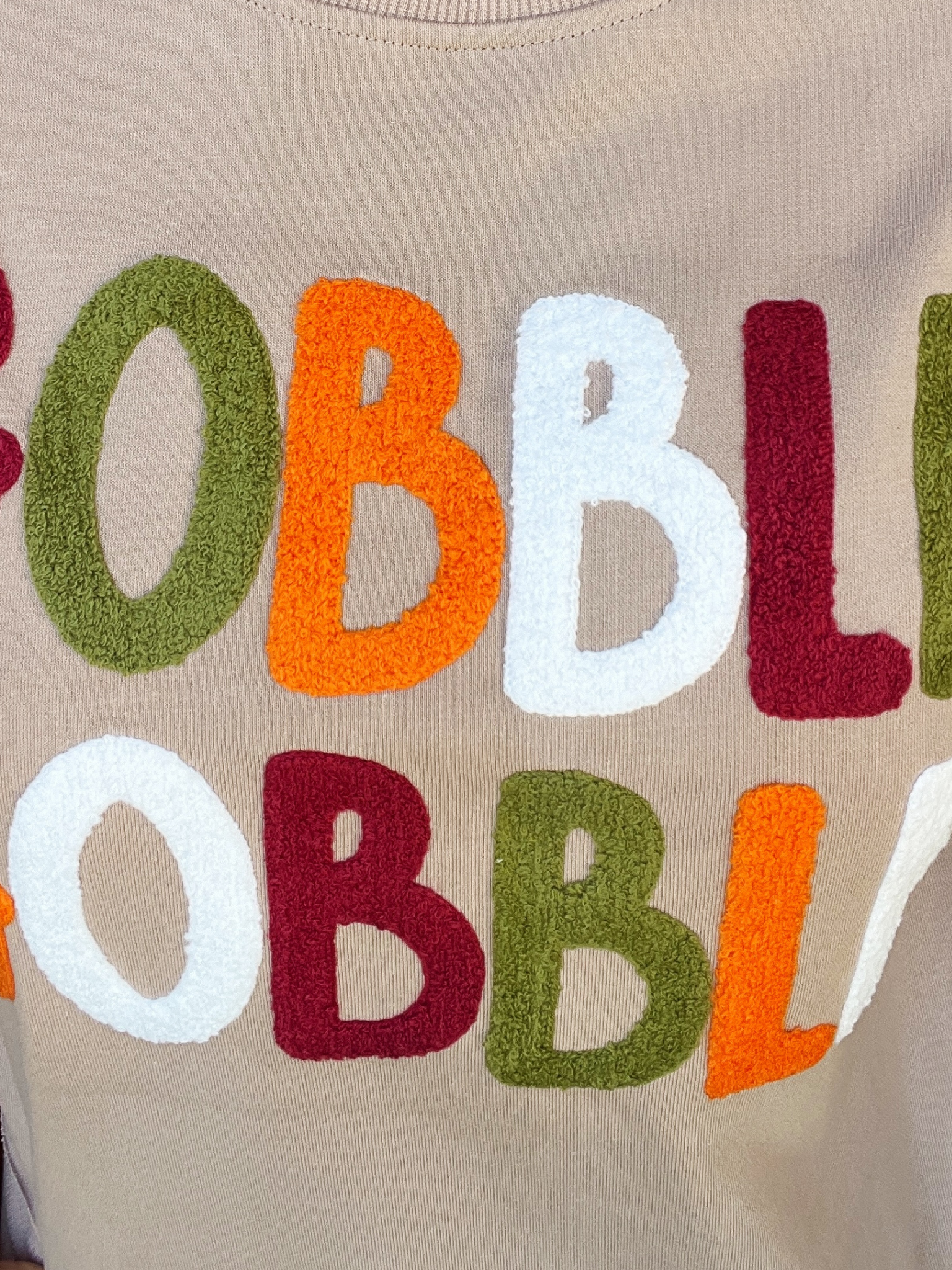 Textured fabric with colorful letters 'OBBL' on a beige background