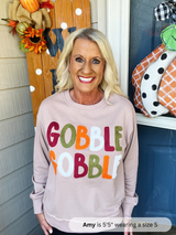 Woman wearing a 'Gobble Gobble' sweater in front of autumn decorations.