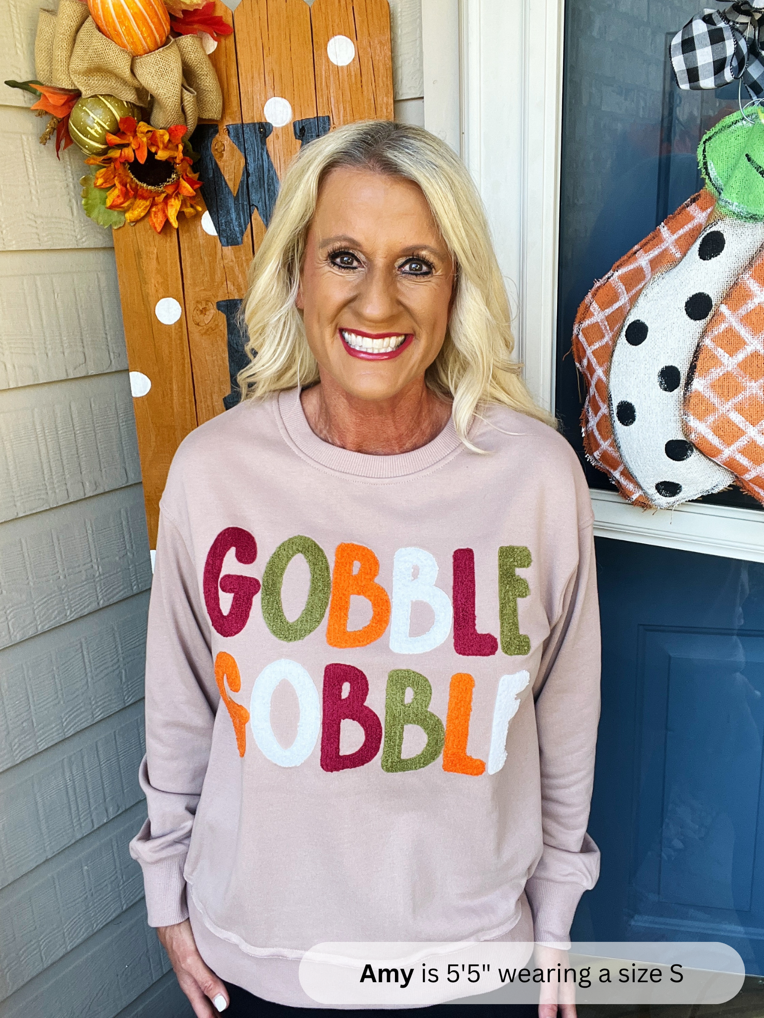 Woman wearing a 'Gobble Gobble' sweater in front of autumn decorations.