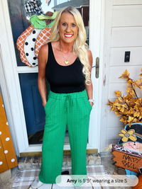 Woman wearing a black top and green pants standing in front of a door with Halloween decorations.