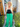 Woman wearing a black top and green pants standing in front of a 'Welcome' sign.