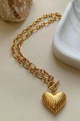 Gold chain necklace with a heart-shaped pendant on a light beige surface.