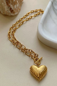 Gold chain necklace with a heart-shaped pendant on a light beige surface.