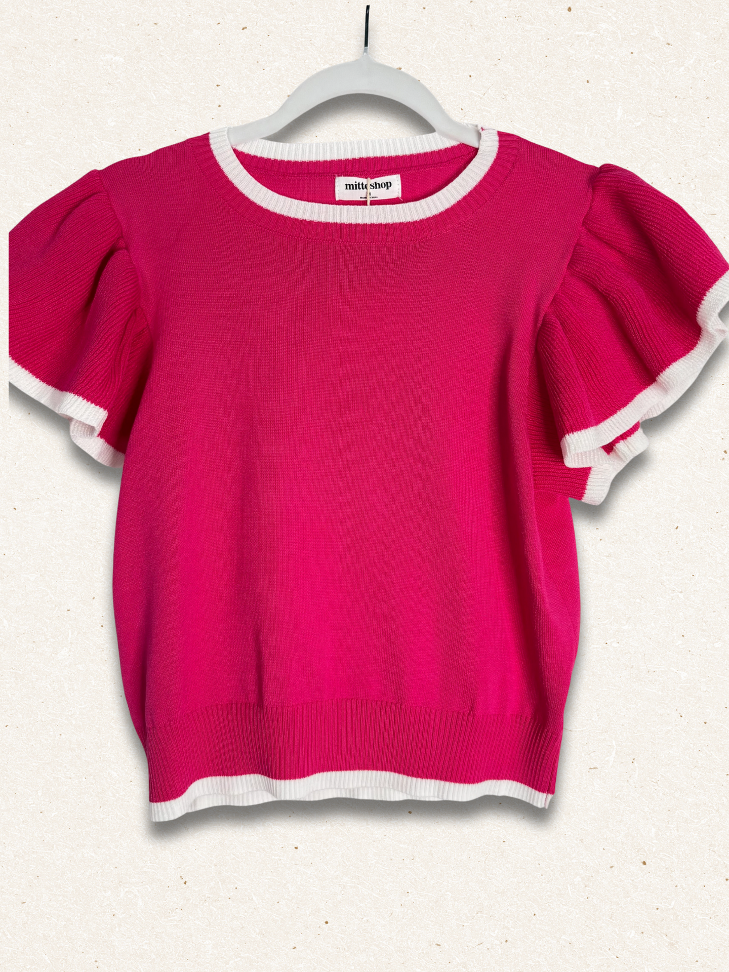 Pink sweater with ruffled sleeves on a hanger against a white background
