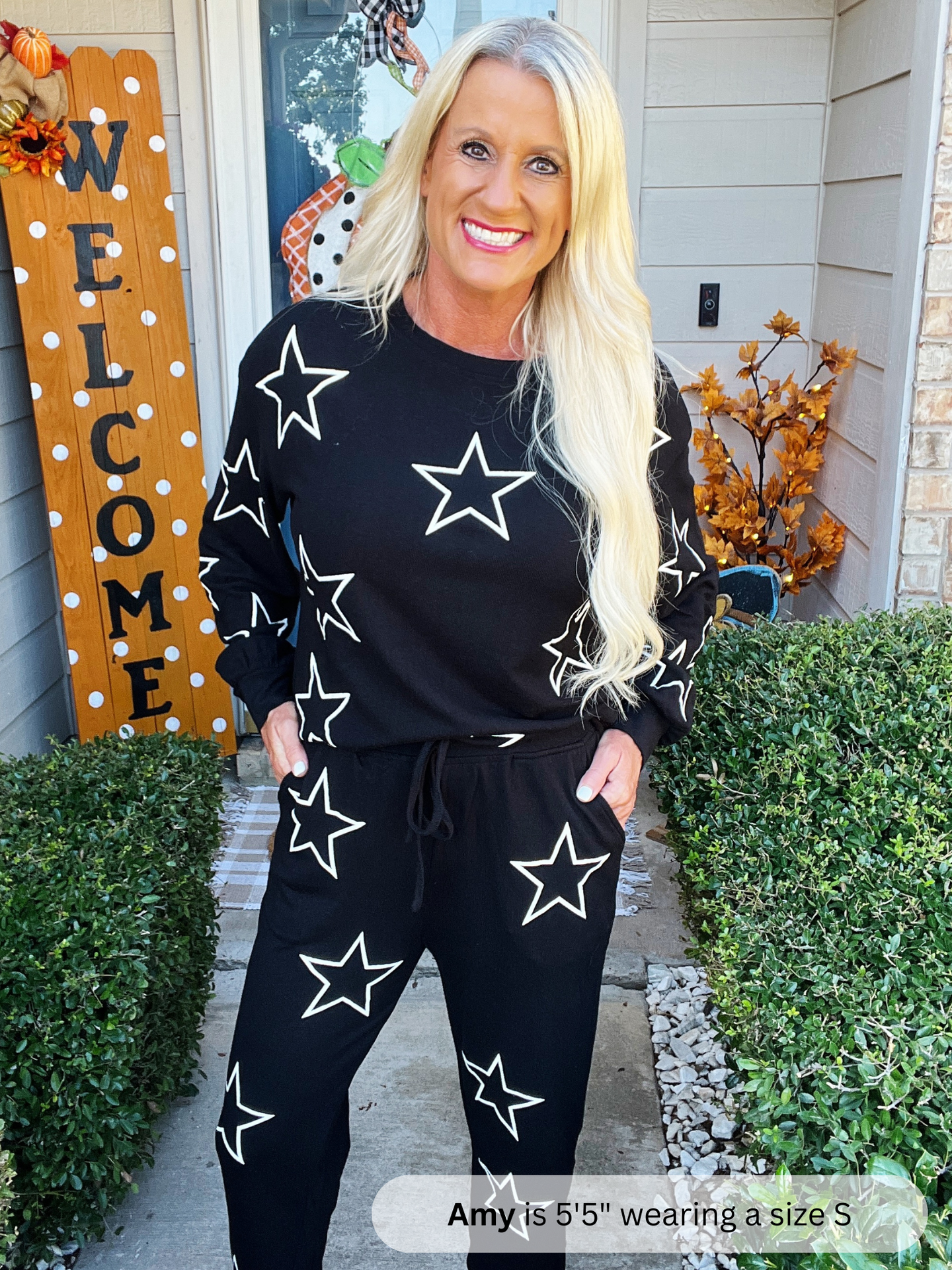 Woman wearing a black outfit with white star patterns standing outside a house.