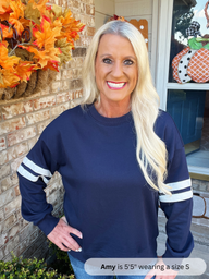 Woman wearing a navy blue sweatshirt with white stripes on sleeves, standing in front of a decorated door.