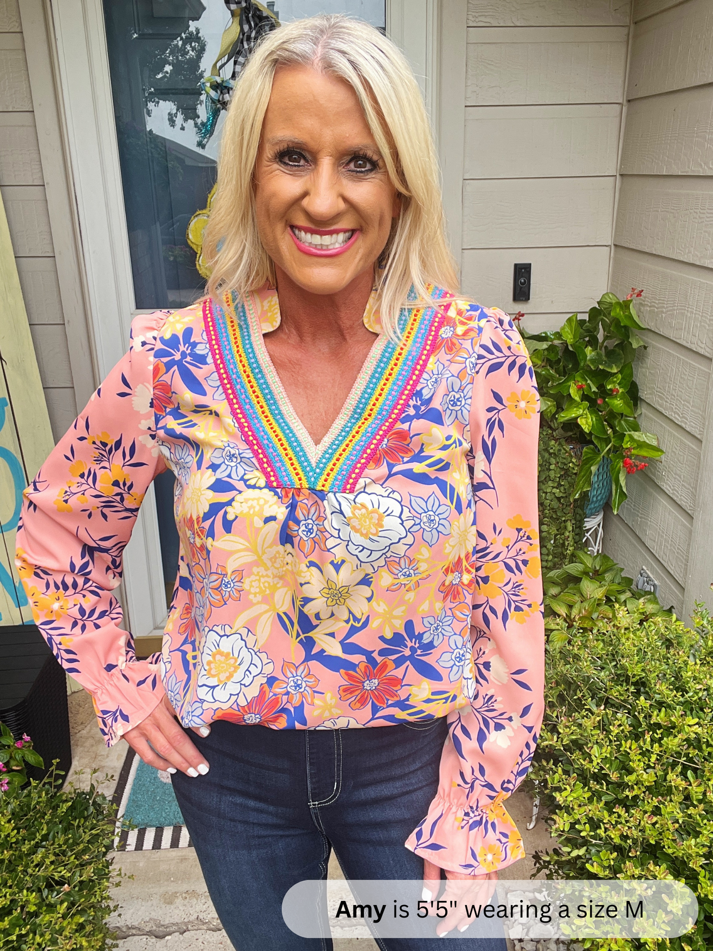 Woman wearing a colorful floral blouse standing outside a house.