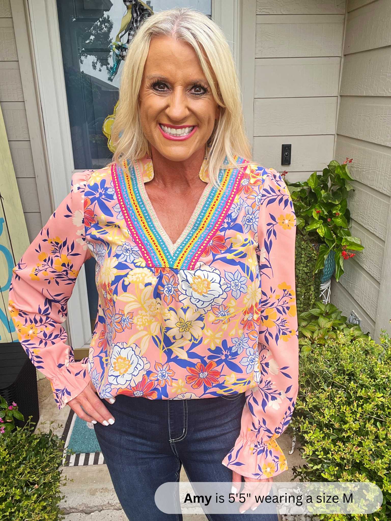 Woman wearing a colorful floral blouse standing outside a house.