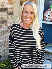 Woman wearing a black and white striped sweater standing in front of a brick wall.