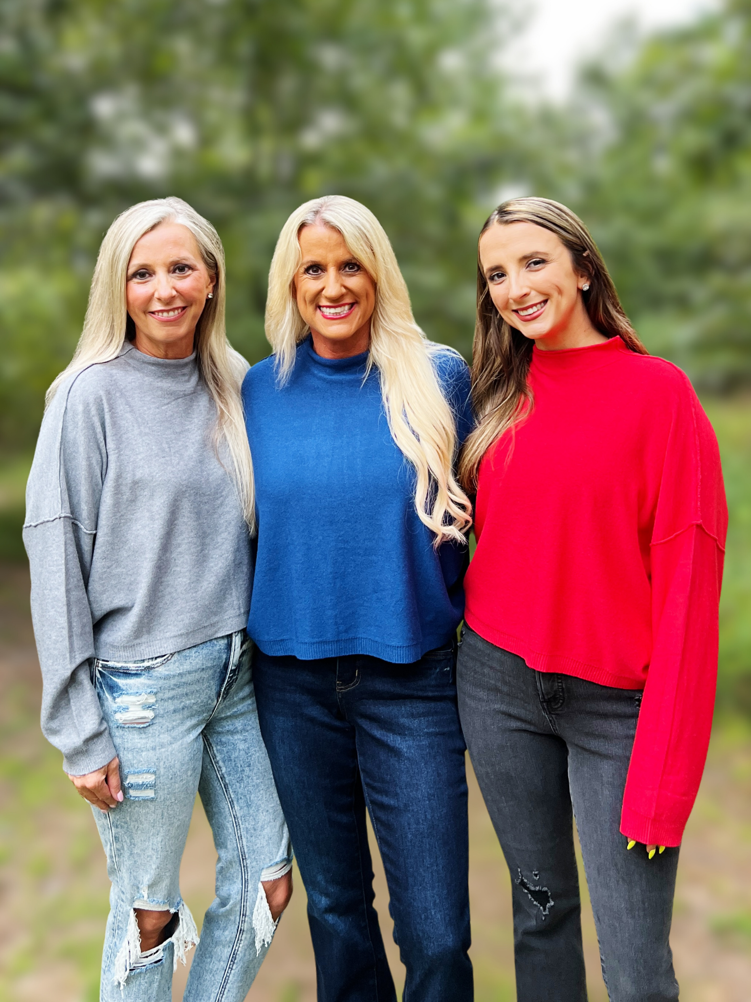 Three women standing together outdoors, wearing colorful sweaters.