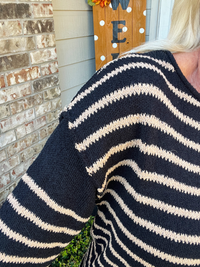 Person wearing a black and white striped sweater with a brick wall and decorative sign in the background.