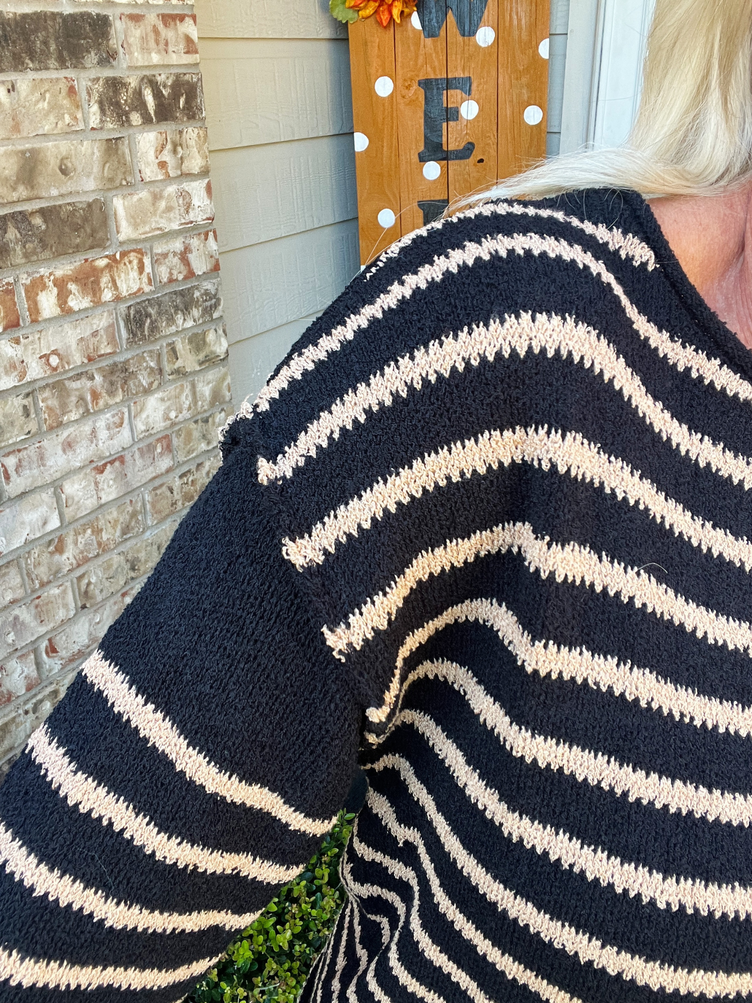 Person wearing a black and white striped sweater with a brick wall and decorative sign in the background.