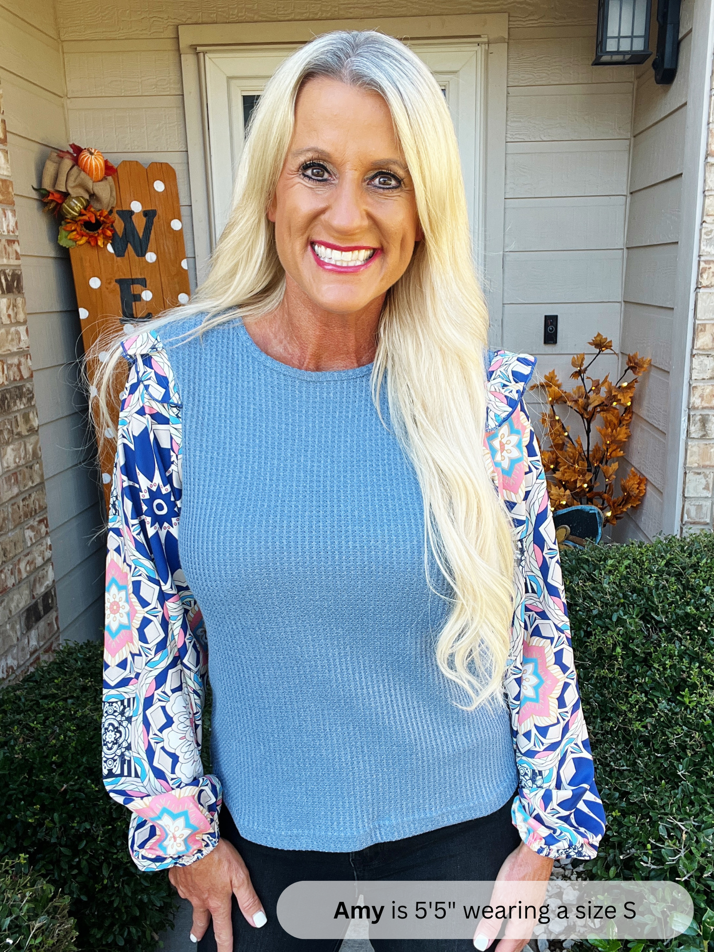 Woman wearing a blue top with floral sleeves standing outside a house.