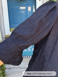 Person wearing a dark blue knitted sweater with a pattern, standing in front of a blue door.