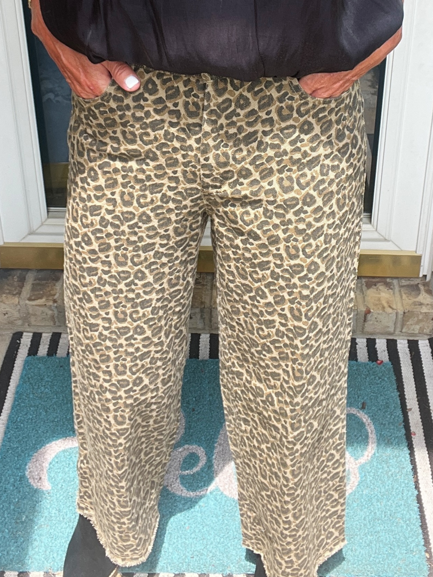 Person wearing leopard print pants standing on a rug with a door in the background
