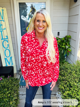 Woman wearing a red floral blouse standing outside a house with 'WELCOME' sign.