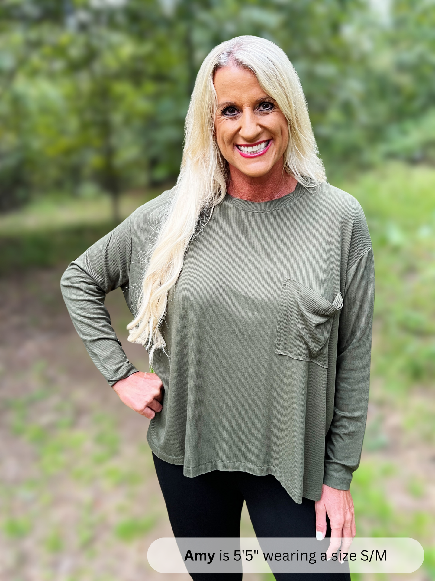 Woman wearing a green long-sleeve top outdoors with a blurred natural background