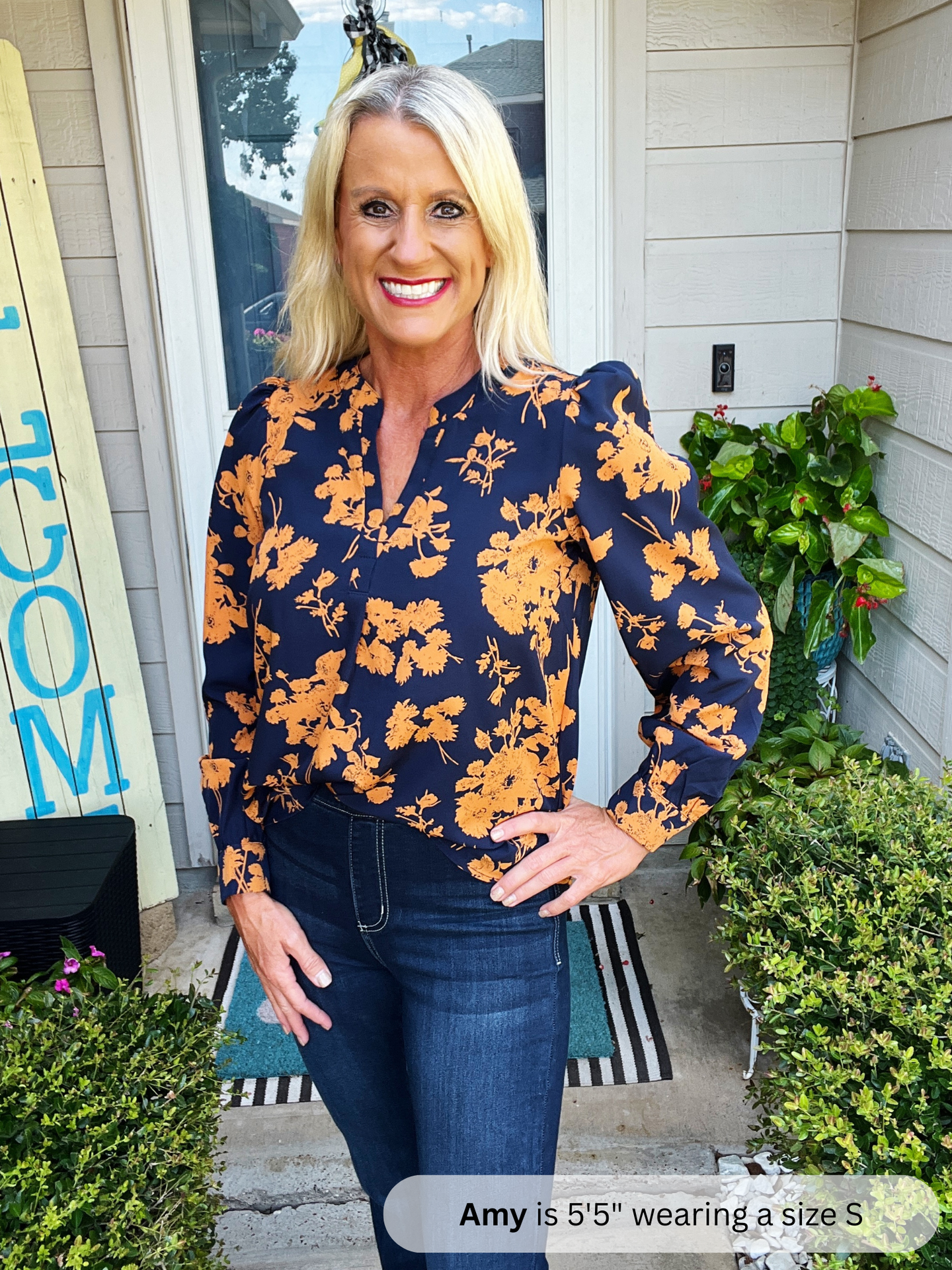 Woman wearing a navy blue floral blouse standing outside a house.