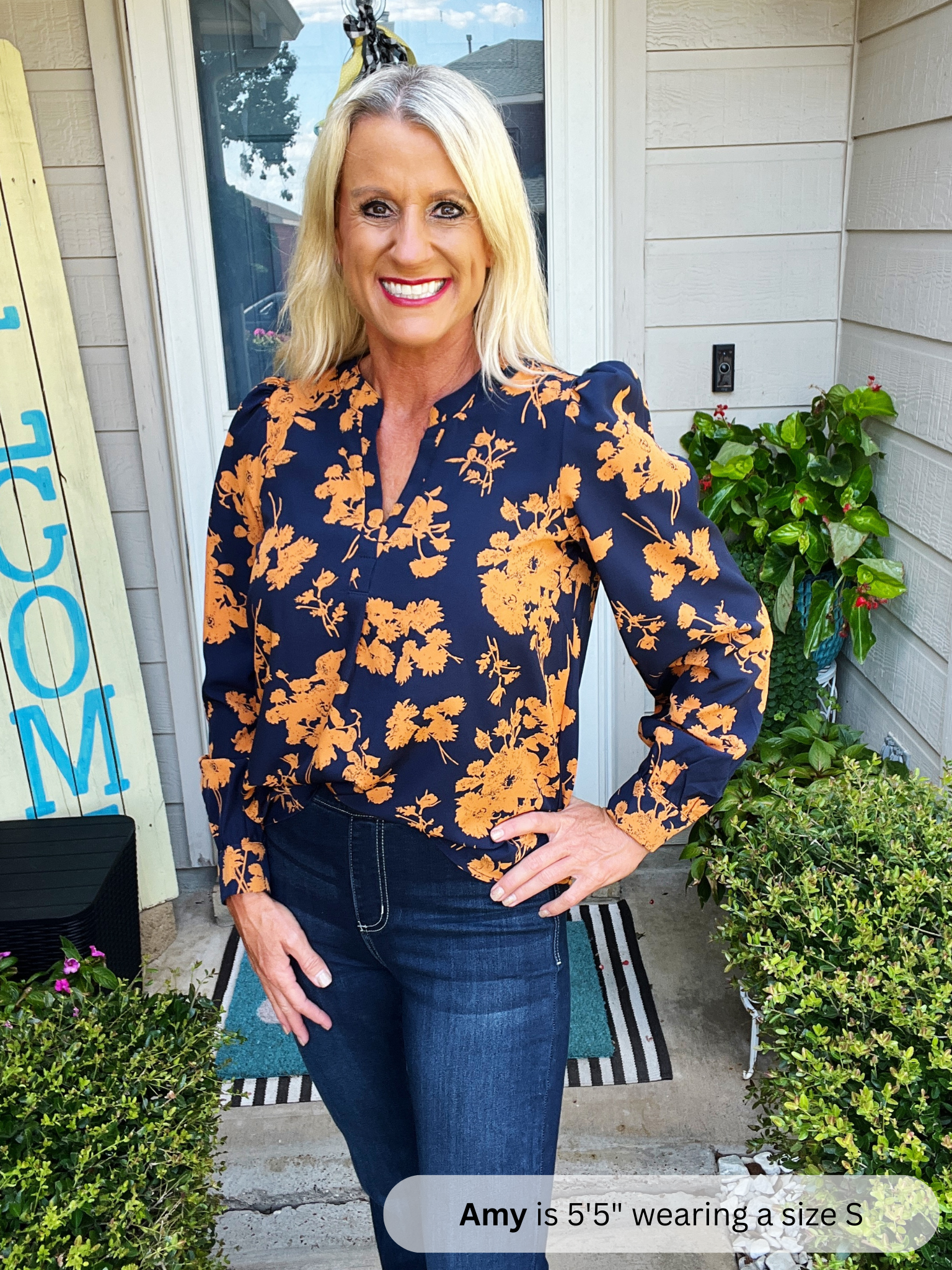 Woman wearing a navy blue floral blouse standing outside a house.