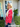Woman in a red floral blouse standing outside a house with a 'WELCOME' sign.
