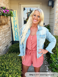/Rust/ Woman in pink romper and denim jacket standing in front of a 'Welcome' sign.