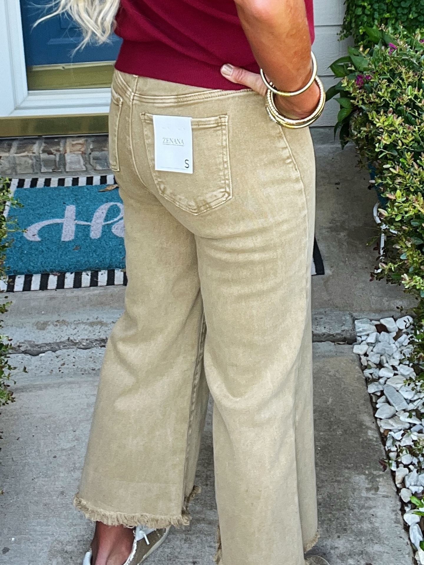 Person wearing beige wide-leg pants with a visible tag, standing on a porch.