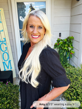 Woman with long blonde hair standing outside a house with a 'WELCOME' sign.