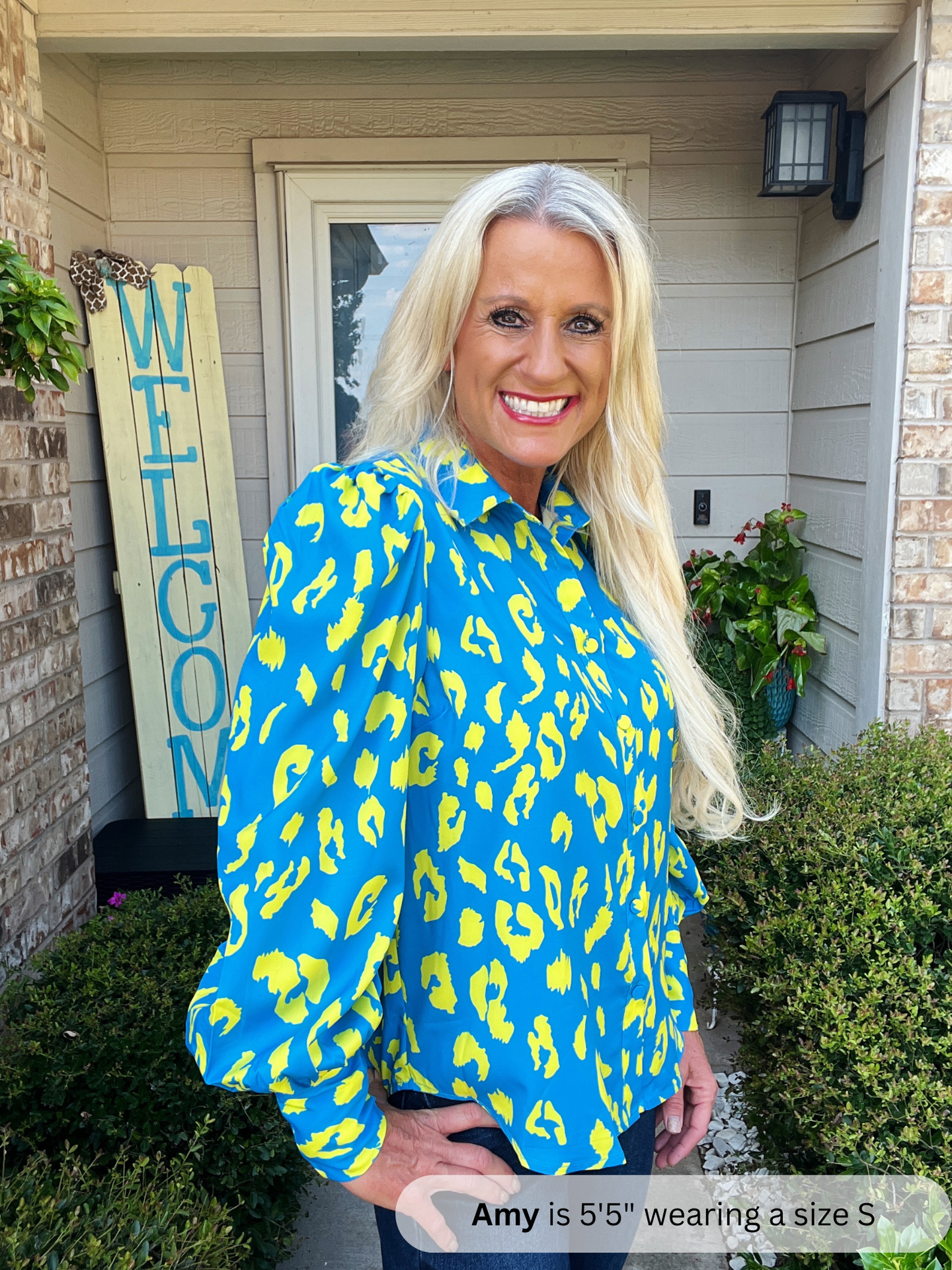 Woman wearing a blue and yellow leopard print shirt standing outside a house.