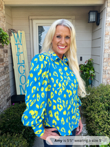 Woman wearing a blue and yellow leopard print shirt standing outside a house.