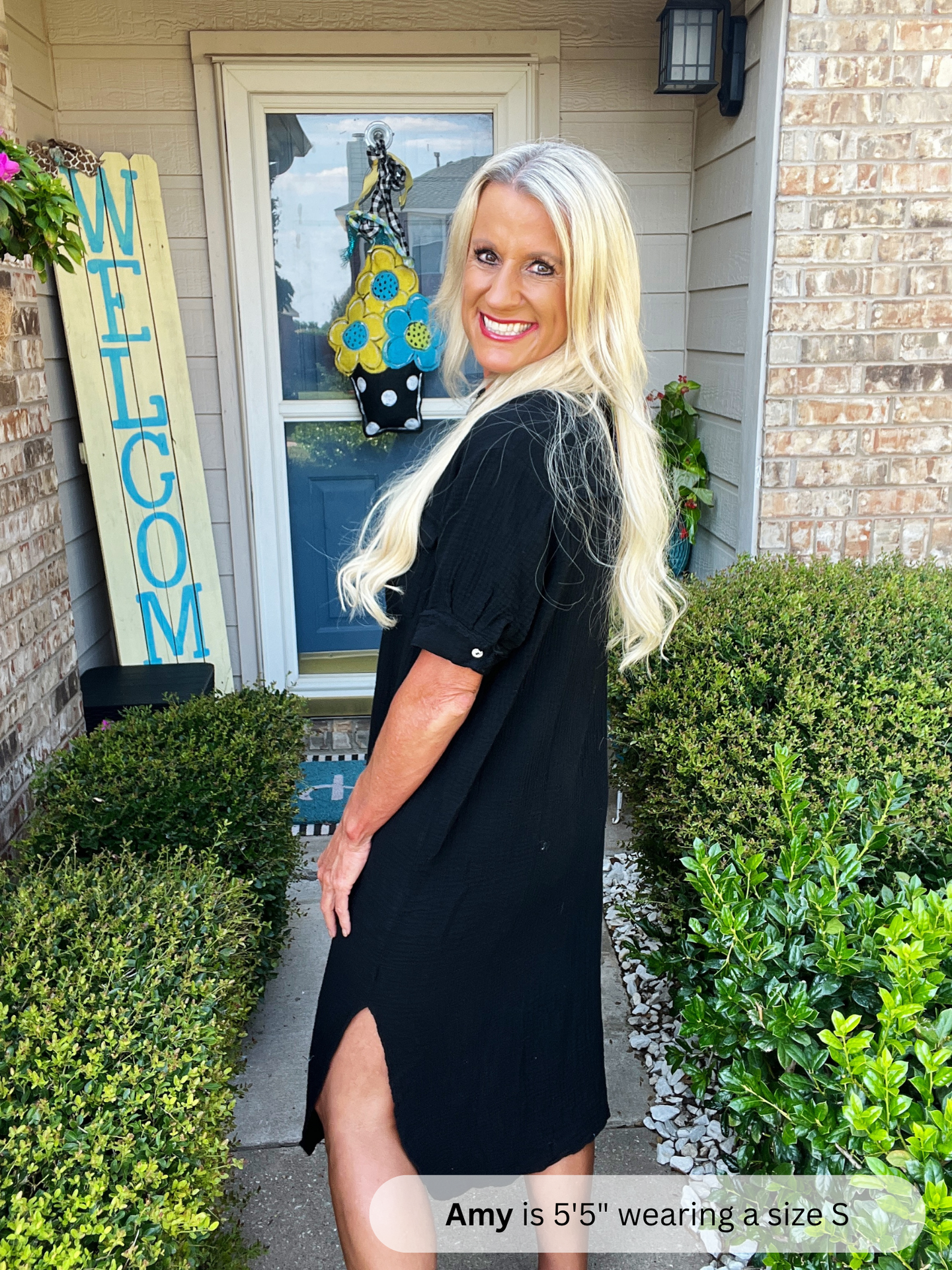 Woman in a black dress standing outside a house with a 'Welcome' sign.