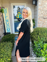 Woman in a black dress standing outside a house with a 'Welcome' sign.