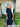 Woman in a black dress standing outside a house with 'WELCOME' sign.