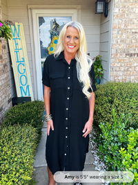 Woman in a black dress standing outside a house with 'WELCOME' sign.