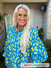 Woman wearing a blue and yellow leopard print shirt in front of a house.