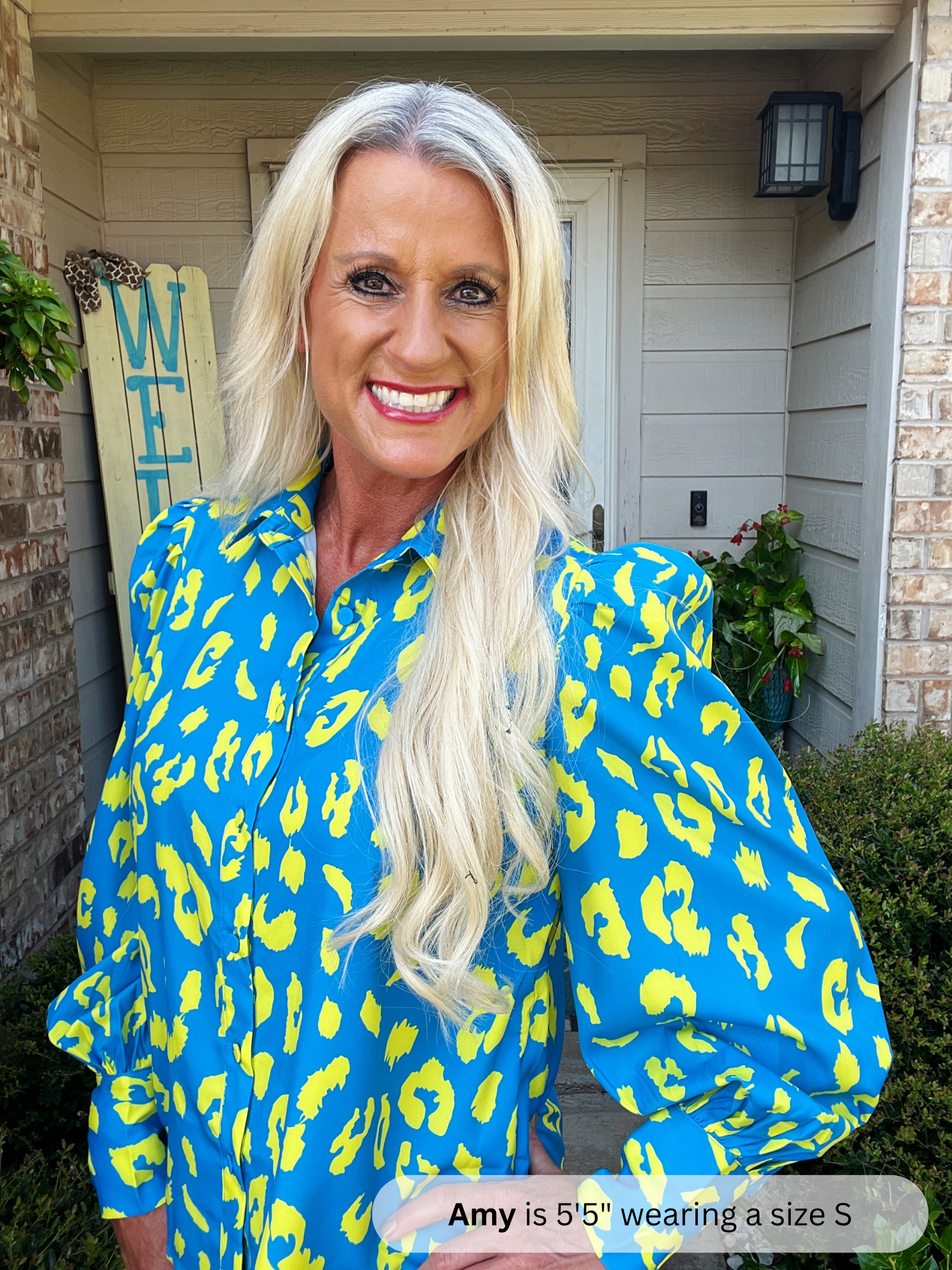 Woman wearing a blue and yellow leopard print shirt in front of a house.