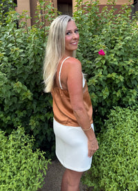 Woman in a white dress standing in front of green bushes with a pink flower.