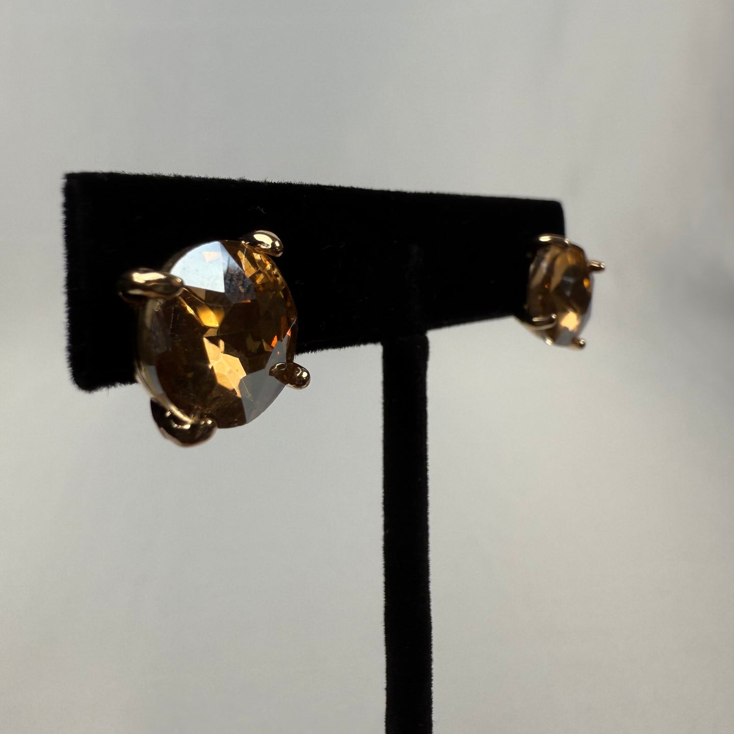 A pair of round, faceted gemstone stud earrings with gold prongs displayed on a black stand against a light background.