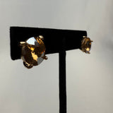 A pair of round, faceted gemstone stud earrings with gold prongs displayed on a black stand against a light background.
