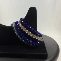A black velvet bracelet display holds three beaded bracelets: one with clear faceted beads, one with dark blue faceted beads, and one with alternating blue and silver beads, against a plain white background.