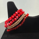 A set of four beaded bracelets displayed on a black stand: two with large faceted red beads, one with small clear rhinestones, and one with small red beads.